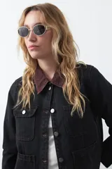 Campera de jean color negro con cuello de pana en tono marrón, cierre frontal con botones metálicos y bolsillos frontales tipo cargo.