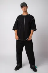 Remera de corte oversize color malva, confeccionada en algodón pesado, con costuras externas visibles en color blanco que recorren el centro, el cuello y los bordes de las mangas.