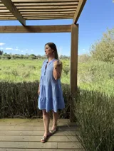Vestido celeste de lino, sin mangas, con cuello mao y botones de nácar. Presenta varios cortes en su largo, aportando movimiento y un toque moderno a este diseño fresco y elegante.