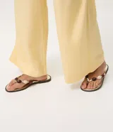 Sandalias planas tipo mule de dedo de la marca Satinato, en color dorado con plantilla metalizada y suela baja. Presenta una tira con aplicaciones decorativas de cuentas de resina en tonos marrones y marfil.