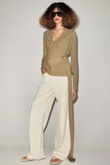 Chaqueta de punto de color tostado, con escote en V y manga larga. Diseño cruzado al frente con cinturón lazada en el mismo tejido y detalle de hebilla metálica circular en el lateral.