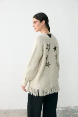 Chaqueta abierta de punto color crema, con diseño de corte recto, bolsillos frontales, flecos en el ruedo y detalle de estrella bordada en uno de los bolsillos.