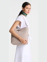 Bolso de hombro tipo hobo, color gris topo, con textura granulada y cierre metálico frontal con forma de palanca.