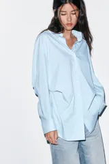 Camisa de corte oversize con estampado de rayas verticales en tonos celeste y blanco. Presenta cuello solapa, escote en pico, manga larga con puños abotonados y un bolsillo de plastrón en el pecho.