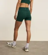 Bermuda deportiva de alta compresión, color verde oscuro, con cintura ancha doblada y detalle de bies lateral en color blanco.