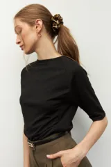 Remera negra de cuello redondo y manga tres cuartos, confeccionada en tela con textura sutil. Presenta fruncidos laterales que aportan caída y movimiento a la prenda.