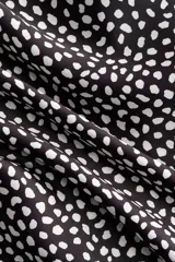 Pantalón negro con estampado de lunares blancos, corte recto y falda cruzada superpuesta con lazada en el lateral.