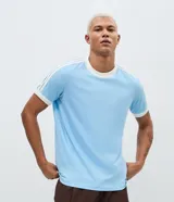 Remera de algodón color celeste con cuello redondo y bordes de mangas en color blanco. Presenta diseño de rayas dobles blancas en los hombros y mangas.