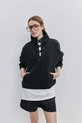 Buzo de algodón negro con calce relajado, cuello alto con cordones cruzados y ojales metálicos, bolsillos laterales y puños y ruedo elásticos.