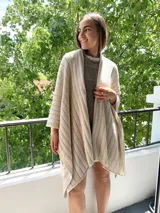 Ruana tejida en punto jersey, color negro con destellos brillantes de lurex. Presenta una etiqueta de cuero sintético con logo en la parte posterior.