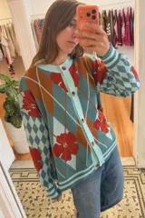 Saco liviano oversize de punto con diseño de rombos argyle y flores celestes sobre fondo marrón, rojo y crema, con cierre frontal de botones y cuello redondo.