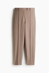 Pantalón sastrero color beige de punto de crepé con pliegue cosido adelante y atrás. Modelo de tiro alto con elástico revestido en la parte posterior de la cintura, cierre y pretina prolongada con botón y cierre oculto de gancho y barra. Piernas ajustadas con tajo en un lateral del bajo.