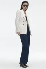 Blazer de corte entallado con cuello y solapa, manga larga y hombros marcados. Presenta un cierre frontal cruzado con botones dorados y bolsillos delanteros con solapa.