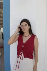 Chaleco tejido sin mangas en color bordó, con escote en V y cierre frontal mediante tiras para anudar. Presenta un diseño corto con terminaciones acanaladas en el ruedo.