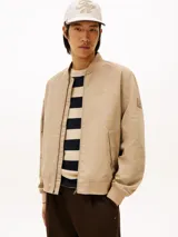Campera estilo bomber Tommy Hilfiger color beige, con cierre frontal de cremallera, bolsillos laterales de ojal, puños y dobladillo de canalé. Cuenta con el logotipo de la marca bordado en el pecho y un parche distintivo en la manga.
