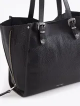 Bolso tipo tote de cuero color tostado con doble asa de hombro, detalles de hebillas metálicas en el frente y cierres laterales decorativos.