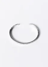 Pulsera esclava abierta de acero quirúrgico plateado con diseño esculpido en los extremos.