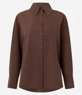 Camisa de corte oversized con estilo sastre, confeccionada en tejido plano. Presenta cuello clásico, cierre frontal con botones, mangas largas con puños anchos y sisas desplazadas.