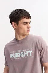 Remera de manga corta color gris topo, con cuello redondo y estampa frontal de estilo urbano con texto en tono claro.