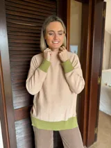 Sweater de punto en color beige con cuello alto y detalles en color verde oliva en los puños y el ruedo. Presenta un diseño holgado con parche de marca en el lateral.