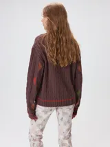 Sweater de tejido de punto trenzado en color marrón, con cuello redondo, puños y ruedo acanalados. Presenta detalles de franjas en color naranja en el cuello y el ruedo, además de apliques de rombos en tonos naranja y verde en las mangas.