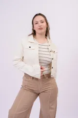 Campera de denim estilo trucker cropped, color beige, con cuello camisero, bolsillos frontales con solapa y botones metálicos.