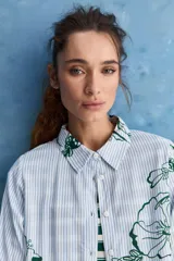 Camisa de calce relajado con cuello clásico, mangas largas con puños elastizados y rayas verticales que aportan un estilo atemporal. Su diseño liviano y versátil cuenta con estampado floral verde sobre fondo de rayas celestes y blancas.