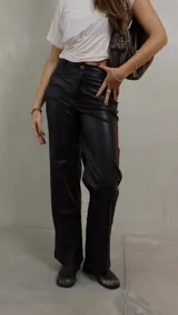 Pantalon de tiro alto confeccionado en cuero sintetico color negro, de corte recto y holgado. Cuenta con cierre frontal, boton metalico, pinzas traseras y pasacintos.