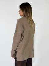 Sweater de punto azul marino con cuello en V, mangas largas con puños acanalados y detalle de línea en color marrón en el cuello y puños. Presenta un pequeño aplique decorativo en la parte inferior.