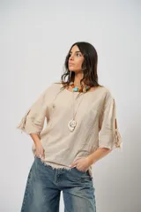 Blusa beige de lino con mangas 3/4 con lazos y detalle de flecos en los puños.