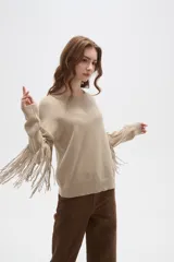 Sweater de punto color beige, con cuello redondo, corte holgado y diseño de flecos largos en las mangas.