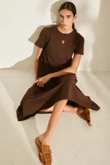 Vestido midi color crudo de manga corta, con corte en la cintura y falda holgada con volados y detalle de pequeño bordado de hongo en el pecho.