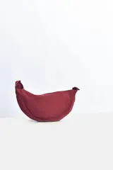 Riñonera tipo bandolera color bordó, con forma de media luna y cierre superior.