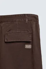 Pantalón cargo de corte relajado confeccionado en tejido de algodón con efecto lavado. Presenta cintura con pliegues frontales, bolsillos laterales con solapa en las perneras, bolsillos frontales y bolsillos traseros con solapa. Cierre frontal con cremallera y botón.