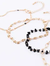 Set de tres brazaletes dorados con diferentes diseños: uno de cadena de eslabones ovalados, uno de cadena fina con pequeñas esferas y uno de cadena con dijes de corazones negros.