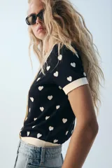 Chaqueta de punto de manga corta con estampado de corazones, cuello polo y cierre frontal con botones en forma de corazón.