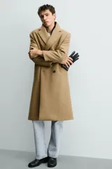 Abrigo largo color camel, de corte relajado (relaxed fit), confeccionado en tejido con mezcla de lana. Presenta cuello con solapas de muesca, manga larga, bolsillos de vivo en cadera, bolsillo interior y cierre frontal de botonadura cruzada.