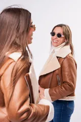 Campera tipo gamulán de cuerina color beige con interior y detalles en corderito blanco. Presenta corte biker, cierre frontal diagonal, bolsillos laterales con cierre y puños con vuelta de corderito.