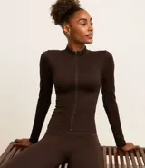 Campera deportiva marrón de corte ajustado, confeccionada en malla de poliamida seamless, con cuello alto, textura acanalada y cierre delantero con cremallera.