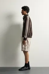 Cazadora relaxed fit de tejido efecto ante color marrón oscuro, con cuello subido y cierre frontal de cremallera. Presenta mangas largas con bandas blancas a contraste en los hombros, bolsillos laterales de vivo, y bordados en hilo blanco en el pecho.