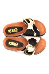 Sandalia tipo zueco con capellada de cuero con pelo estampado animal print de vaca en blanco y negro. Presenta una hebilla metálica dorada grande en el empeine, plantilla anatómica de corcho y suela de goma negra.
