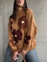 Sweater de punto grueso color camel, con diseño de flores grandes aplicadas en tonos marrones y centro crema. Presenta cuello redondo alto, mangas largas con hombros caídos y terminaciones acanaladas.