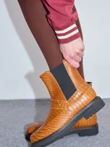 Bota de cuero color tostado con textura símil cocodrilo, diseño tipo Chelsea con elásticos laterales negros, costuras pespunteadas y suela dentada de goma.