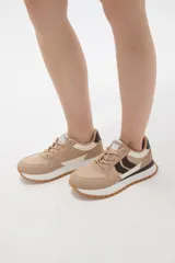 Zapatilla deportiva de diseño urbano, combinando paneles de tela blanca y gamuza sintética en tono gris claro. Cuenta con cordones grises, suela de plataforma con entresuela blanca y base dentada en color caramelo.