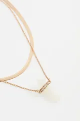 Collar doble de metal dorado, compuesto por una cadena tipo serpiente y una cadena fina con dije de piedra de resina blanca en forma de punta, decorado con pequeños cristales incrustados.