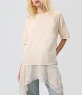 Remera oversized de algodón color beige, de manga corta y cuello redondo, con superposición inferior liviana, bajo asimétrico y aplicación de encaje.