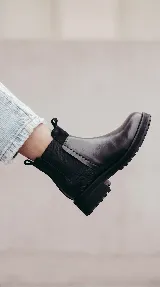 Bota tipo Chelsea de cuero negro con paneles elásticos laterales y suela track dentada. Presenta un diseño minimalista con tirador en la parte trasera.