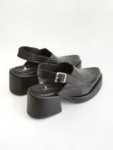 Zapato tipo slingback color negro, con plataforma y taco cuadrado. Presenta una puntera cuadrada y cierre con hebilla metálica en la tira trasera.