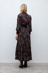 Vestido midi de corte camisero con estampado paisley en tonos oscuros, manga larga con puños ajustados y cierre frontal de botones. Presenta un diseño fluido con falda de volantes en el ruedo.