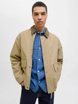 Campera utility de manga larga color beige, con cuello camisero de pana marrón. Tiene cierre de botones, dos bolsillos frontales con solapa y un interior forrado en poliéster reciclado. Cuenta con acabado repelente al agua.